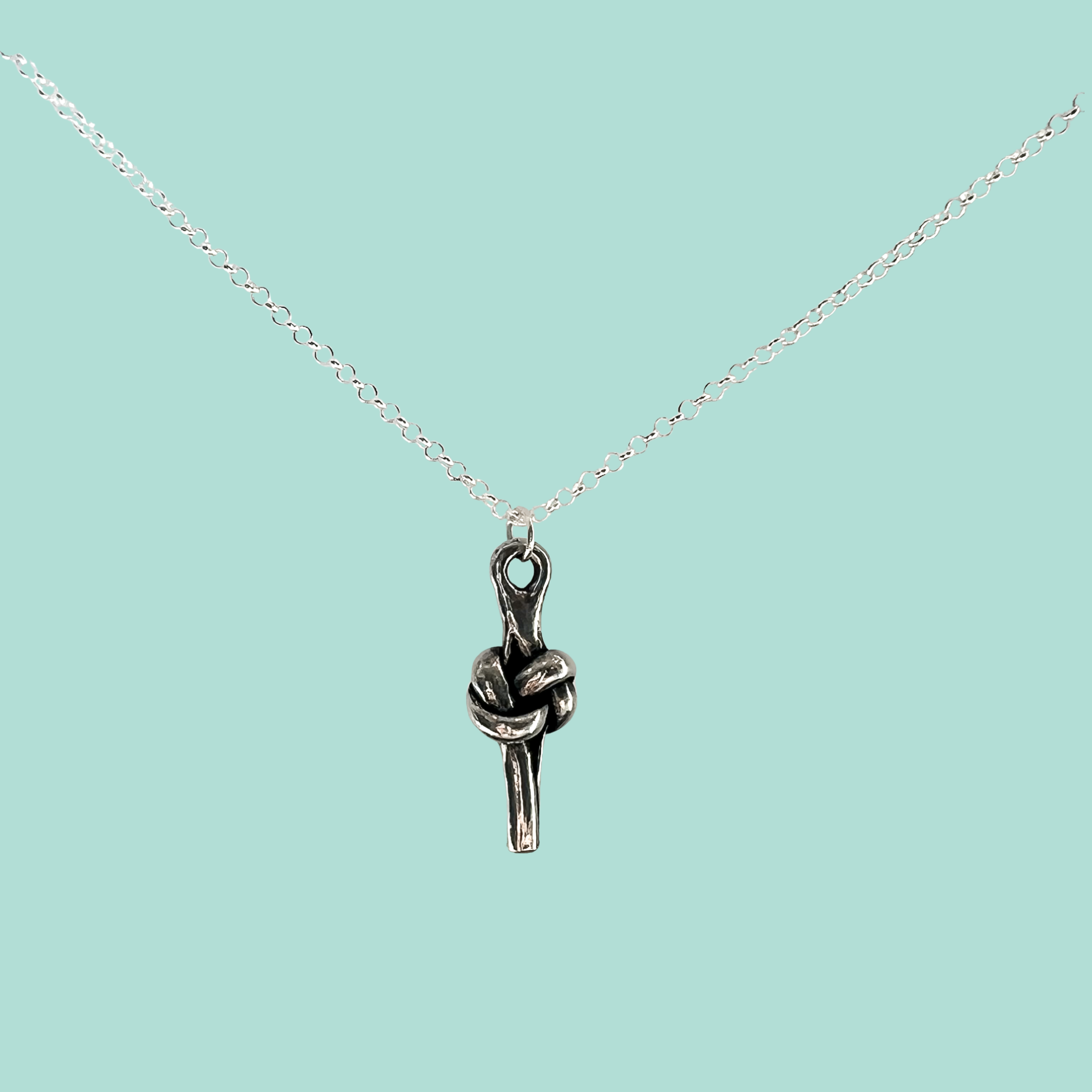 A silver chain necklace with a small pendant shaped like a love knot, shown on a solid light aqua background.