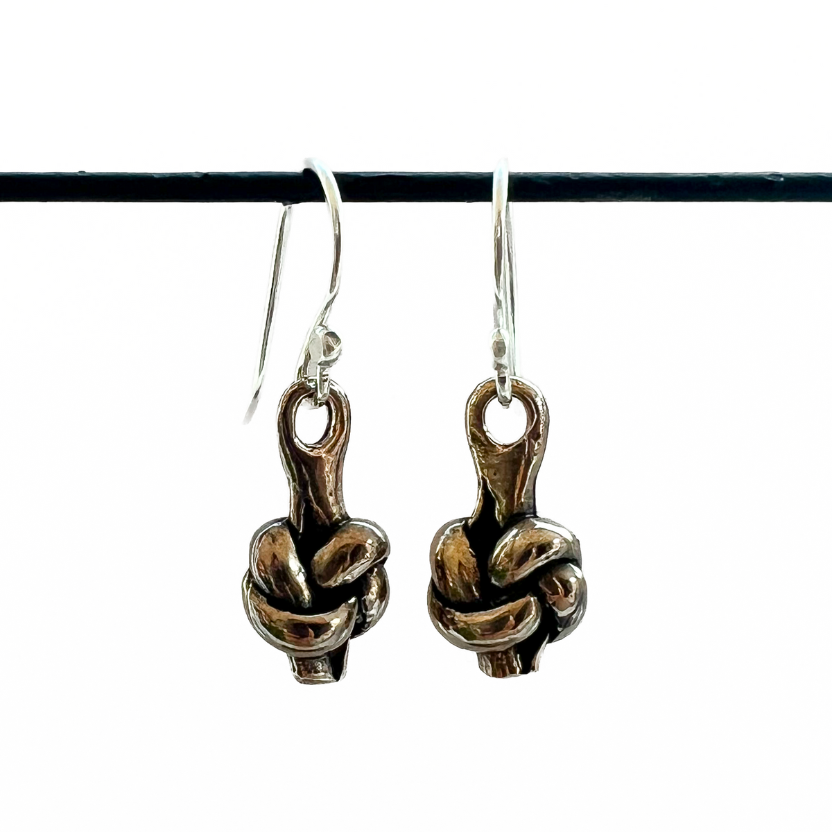Pair of bronze knot charms hanging from silver ear wires on a white background.