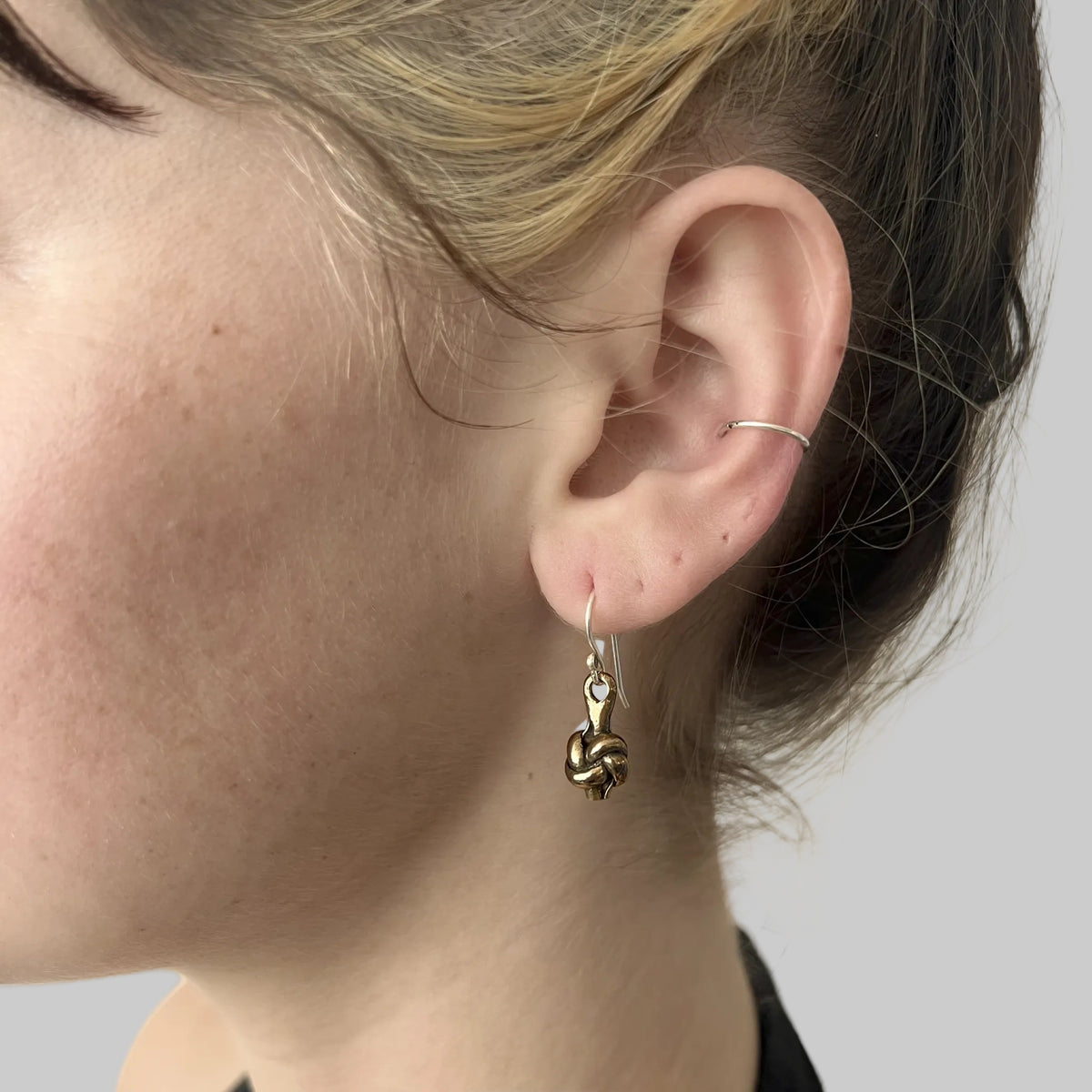 Bronze love knot earrings on model, close up of ear and jawline.