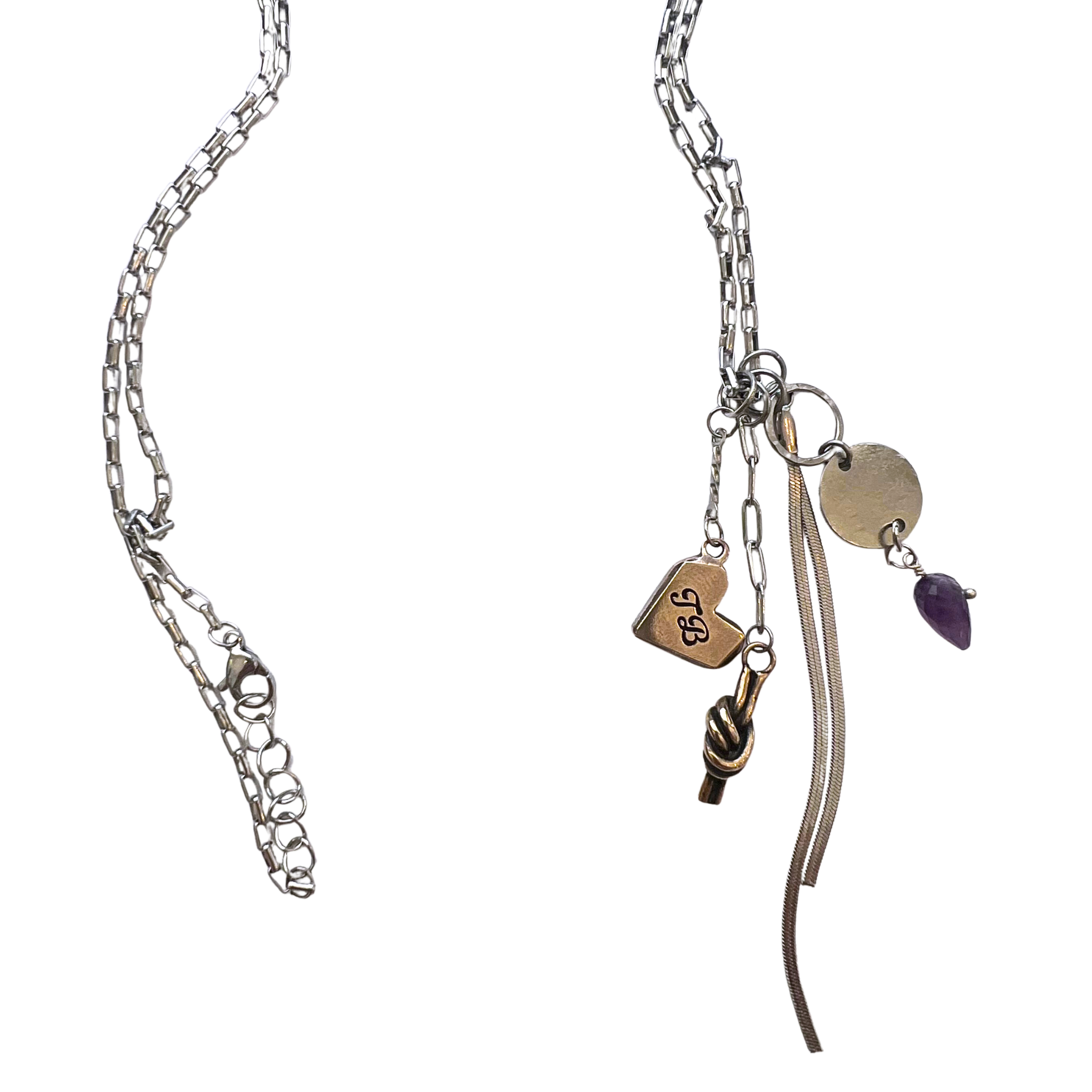 A silver-toned chain necklace with multiple dangling charms, including a heart engraved with 'J&J', a small knot charm, a round disc charm, a flat oval charm, and a small purple teardrop bead, shown on a plain white background.