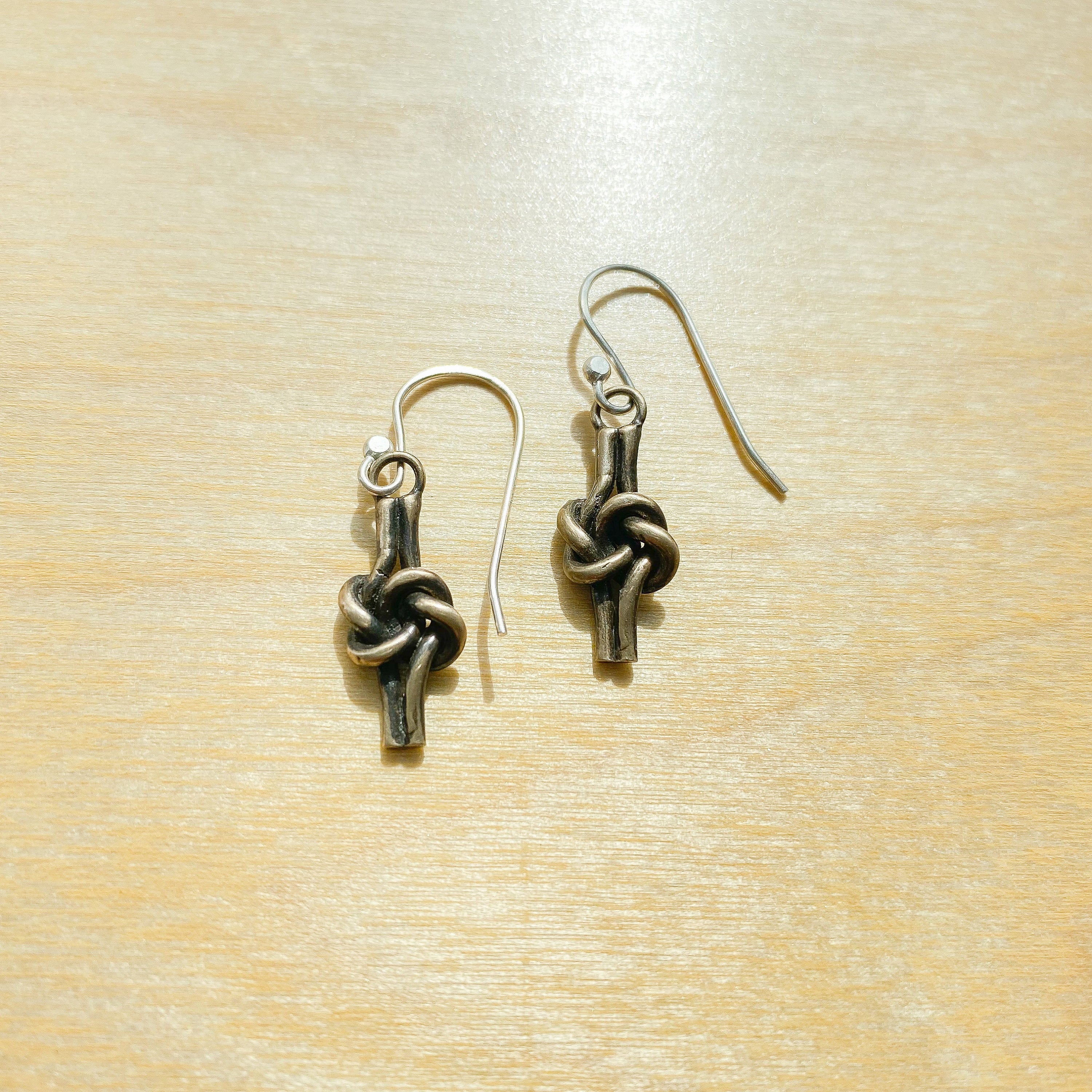 Bronze love knot earrings with silver ear wires laying on wood background.