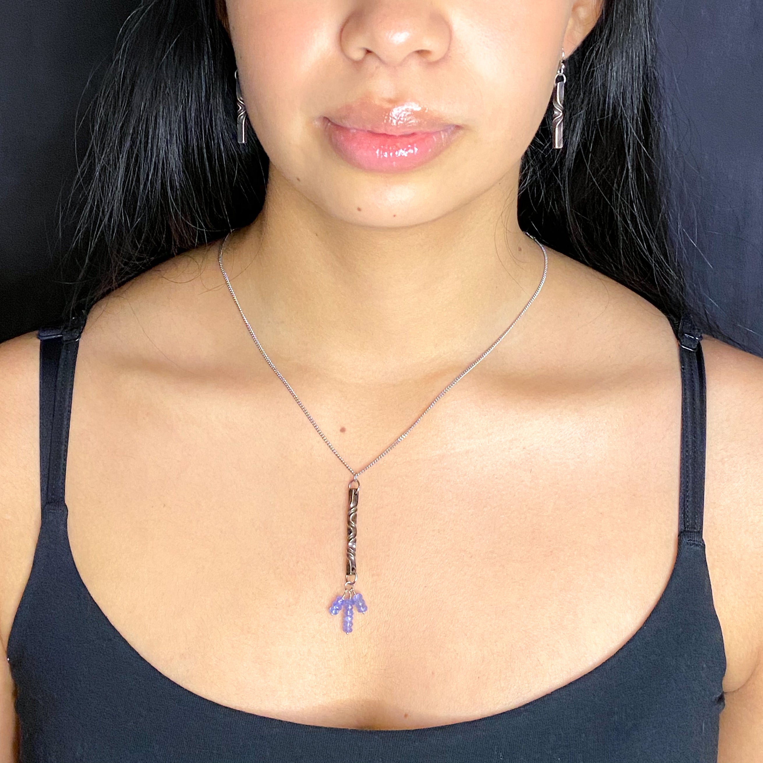 A person wearing a bronze and tanzanite pendant necklace with a matching earrings, on a black background.