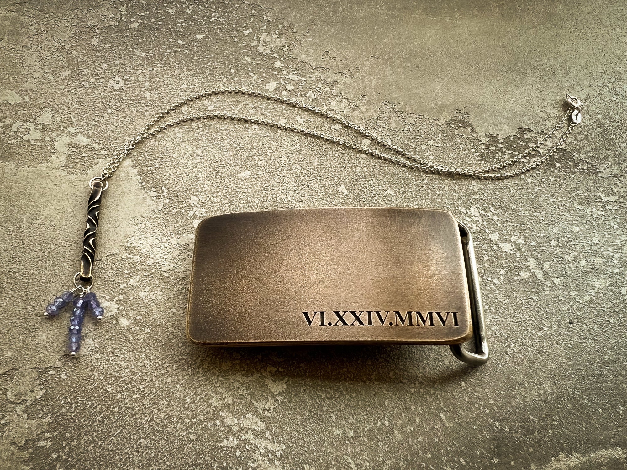 Bronze belt buckle with engraved Roman numerals and a chain with charms on a textured surface