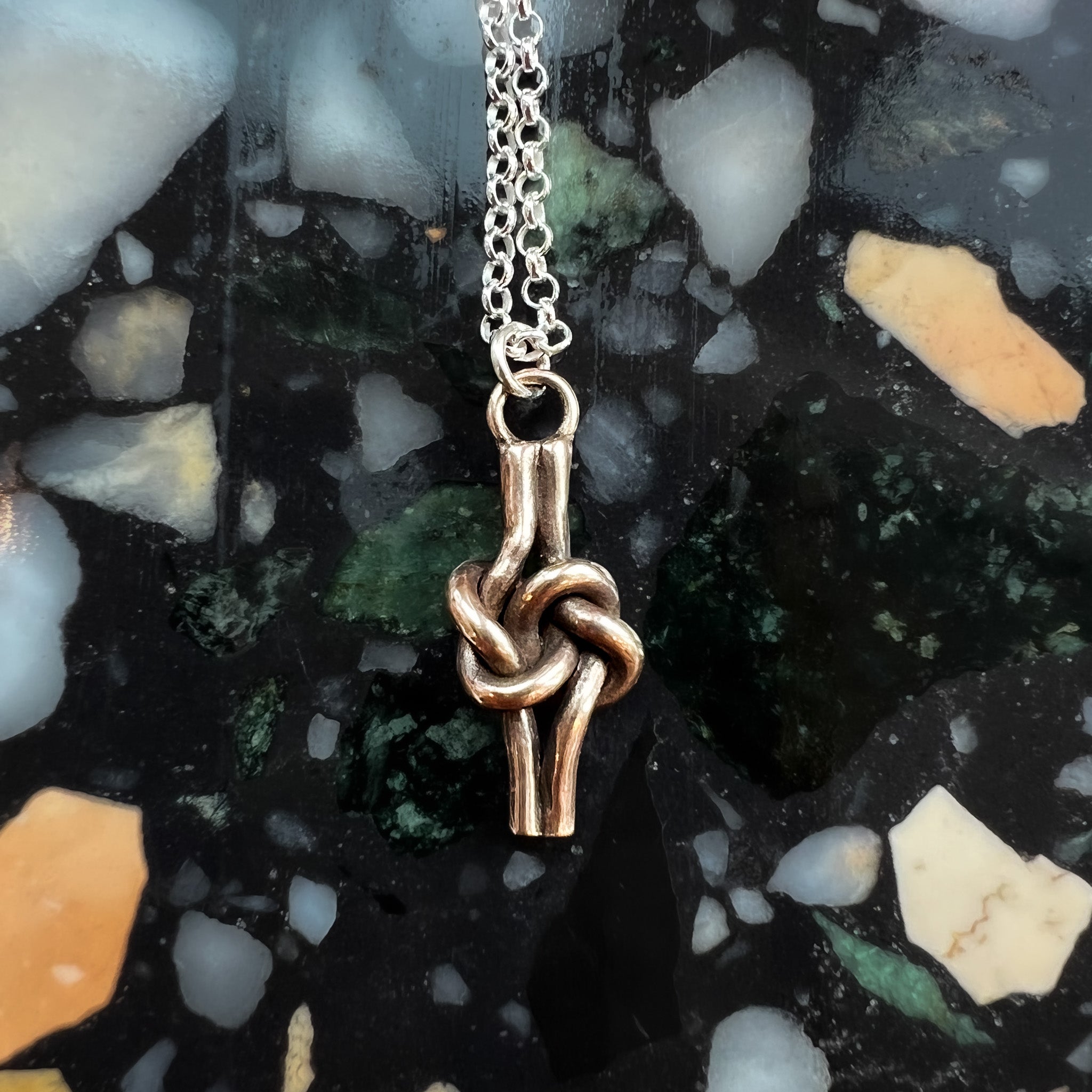 Close up of bronze knot pendant on multicolored stone background. 