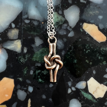 Close up of bronze knot pendant on multicolored stone background. 