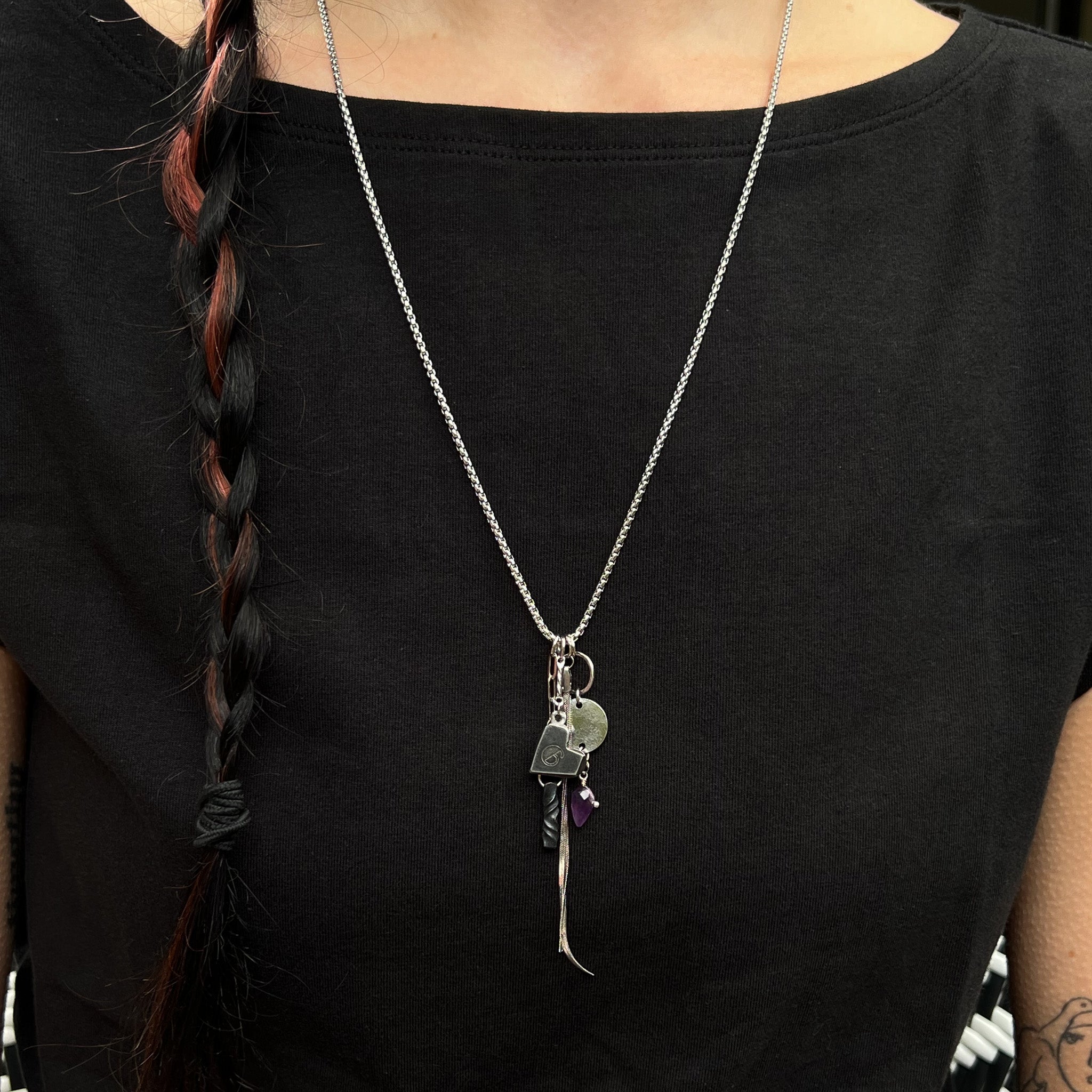 Multiple stainless and iron charms on a stainless chain on model in black shirt.