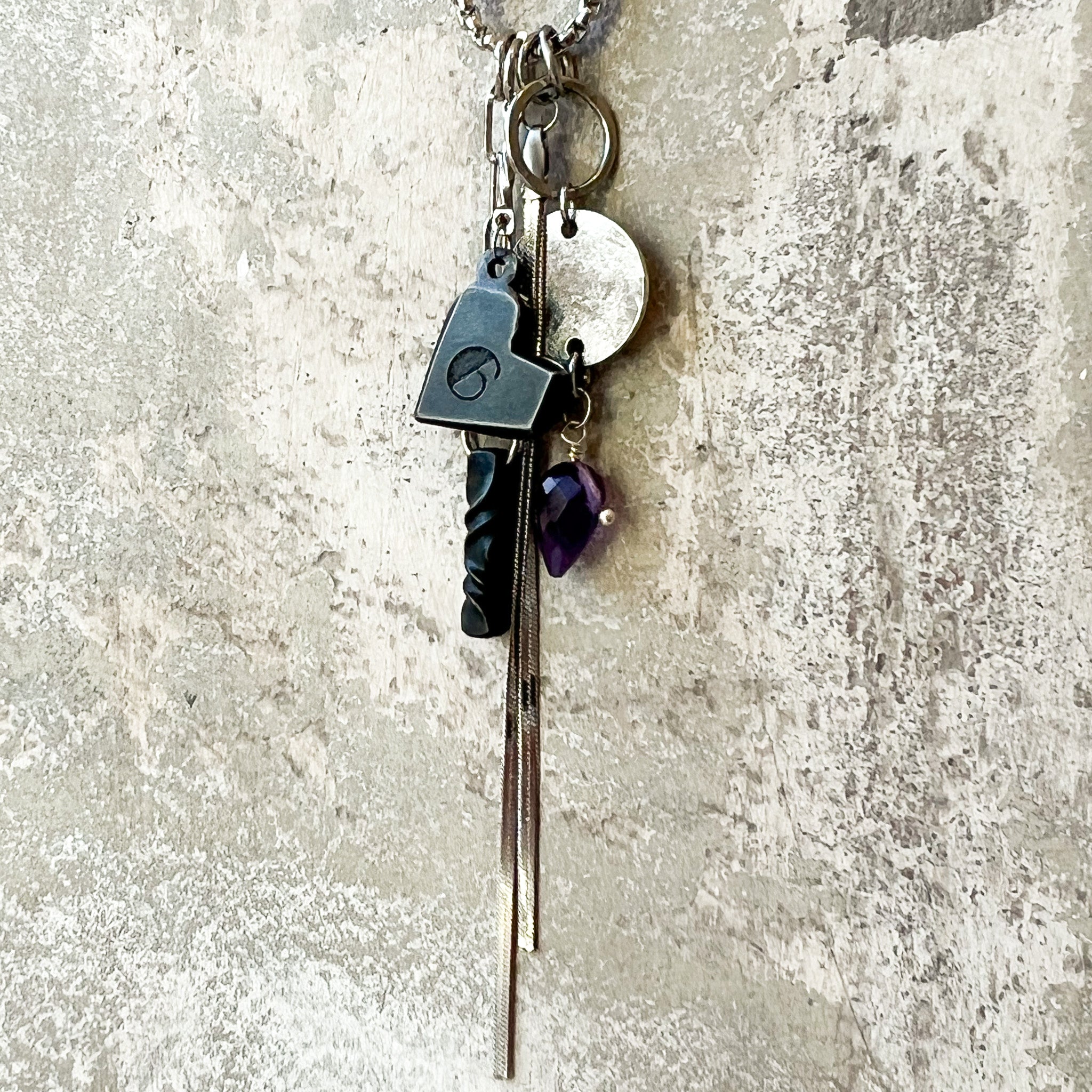 Iron heart, stainless gem drop charm, iron twist and snake chain tassel charms together on plaster background.