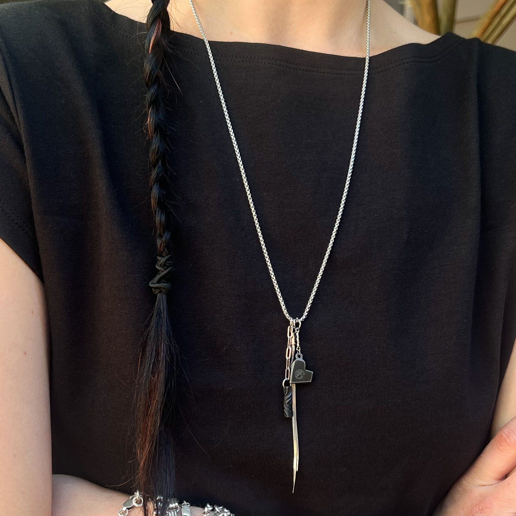 Person wearing a black top with a stainless chain featuring iron engraved heart charm and twist and tassel charms.
