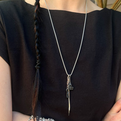 Person wearing a black top with a stainless chain featuring iron engraved heart charm and twist and tassel charms.