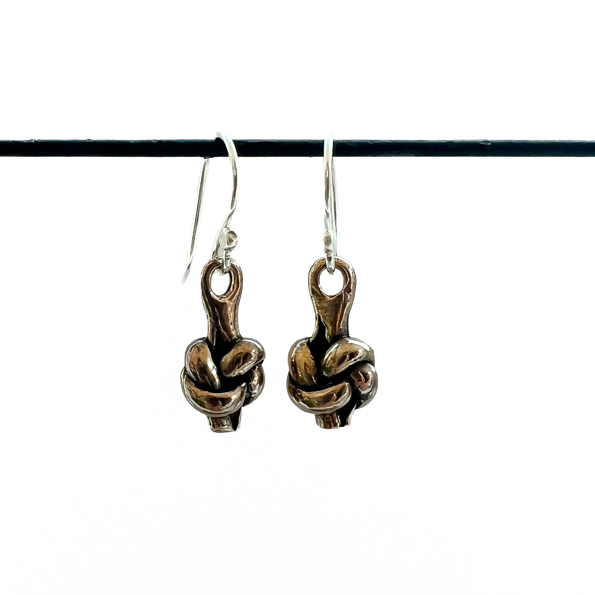 Pair of bronze knot charms hanging from silver ear wires on a white background.